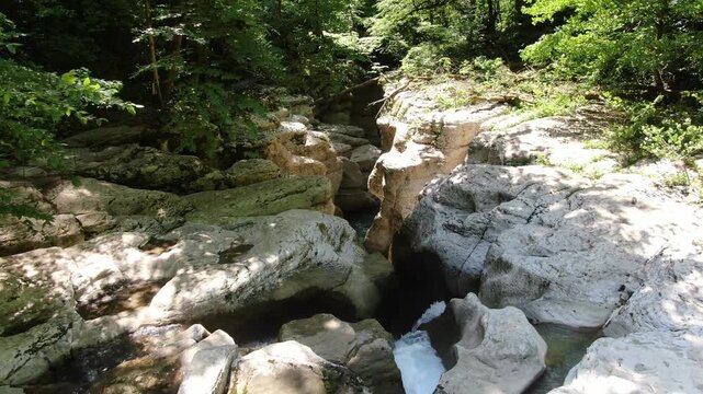 Scenic view of the crystal-clear Khosta River flowing through the deep white rock canyon and lush green forest in Sochi, Russia.