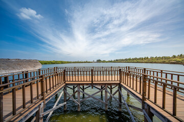 Obraz premium Wooden pier over a calm tropical lagoon with clear blue sky and soft clouds. The empty boardwalk creates a peaceful atmosphere, ideal for travel, vacation, and resort concepts in a natural coastal env