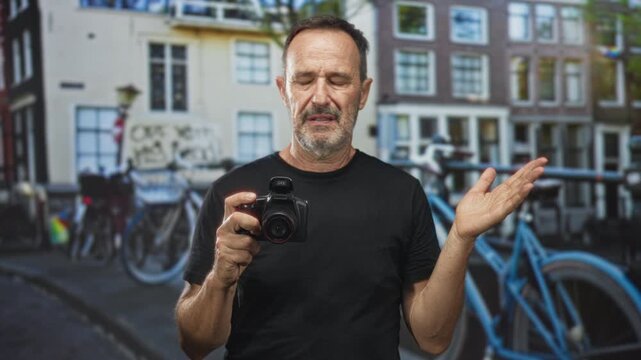 Man holding dslr camera, eyes closed and right hand raised in questioning gesture on a street lined with bicycles and buildings; confusion travel reflection.