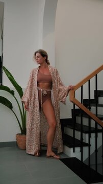 Elegant woman wearing luxury kimono robe over  swimsuit in modern tropical villa.