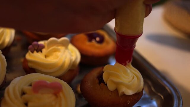 A pastry chef skillfully decorates cupcakes with smooth white frosting using a piping bag, creating an exquisite dessert in a bustling professional kitchen filled with mouth-watering aromas. Slow moti