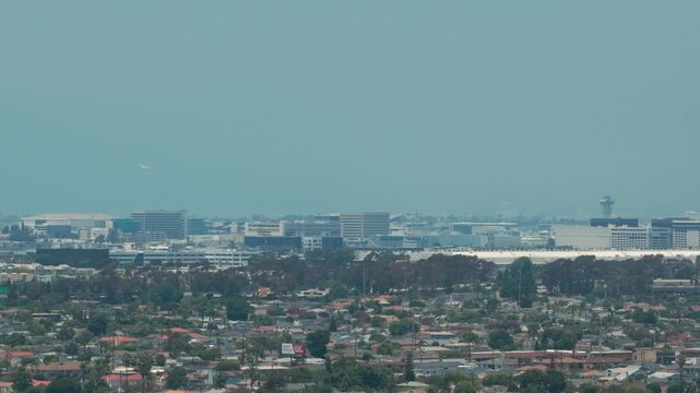 Telephoto panning aerial shot of a plane taking off at LAX on a hazy day as seen from Hawthorne, California. 4K