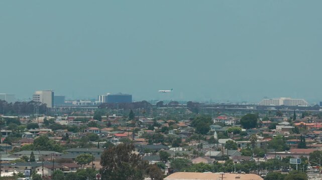 Aerial telephoto panning shot of an airplane landing at LAX in the distance as seen from Hawthorne, California. 4K