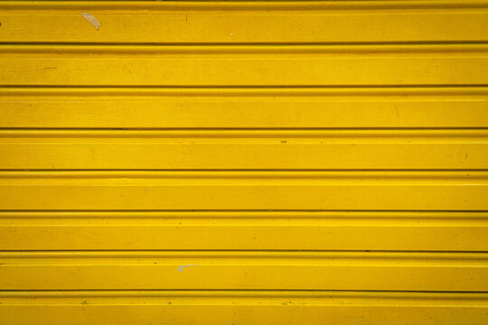 Yellow metal rolling shutter door with horizontal lines creating a clean industrial texture and abstract background.