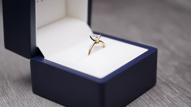 Hands opening a Engagement ring box. Wedding ring in a box being opened up. Engagement ring revealed, marriage proposal. Emerald cut diamond yellow gold knife edge