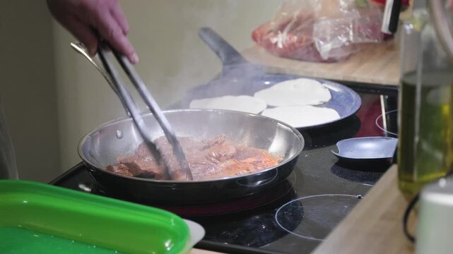 Close up cooking footage showing slow motion of man flipping arrachera beef in kitchen while preparing homemade arrachera steak tacos in a home kitchen