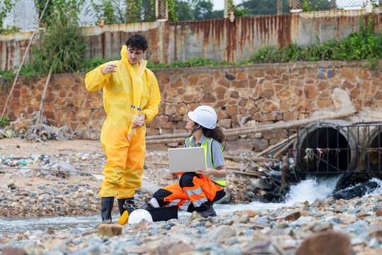 Environmental scientists in hazmat suit and safety gear testing water quality at drainage pipe, Researchers in protective suit checking chemical contamination and water quality near wastewater pipe