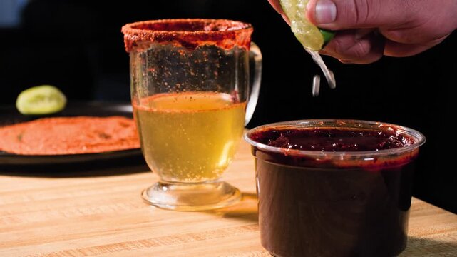 Close up cooking footage showing man adding lime to chamoy sauce with beer and tajin in background during a homemade chamoy sauce recipe prepared from scratch