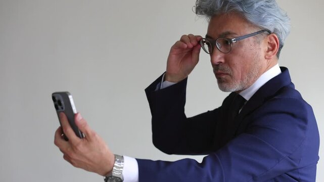 スマートフォンの画面が見えにくい老眼のシニアビジネスマン