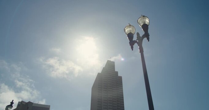4K handheld cinematic view from the San Francisco Embarcadero walkway looking toward urban building and lamppost along the waterfront with a harsh Sun Flare.