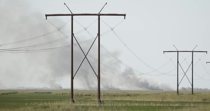 4K footage of multiple wildfire hotspots burning across the Florida Everglades in Broward County. Smoke rises beyond sawgrass marshes, Powerlines in foreground.