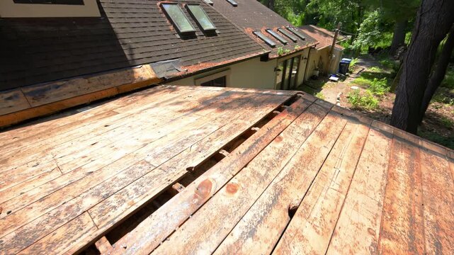 Wide view of an aging residential roof during a complete roof replacement project. Worn wooden roof decking