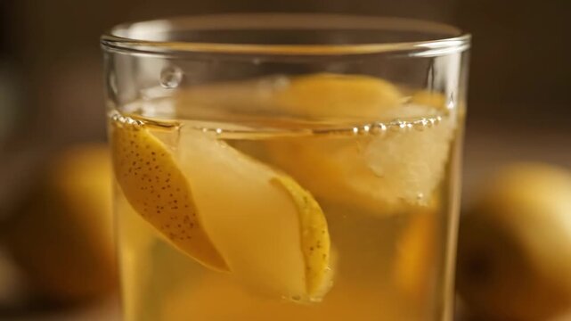 Close-up of refreshing golden pear iced tea or cocktail served in a glass with fruit slices and ice cubes on a dark, moody background.