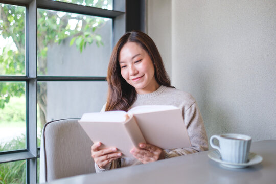 Portrait image of a woman reading a book with coffee cup on the table