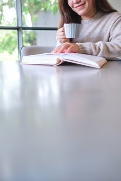 Vertical closeup image of a woman reading a book and drinking coffee