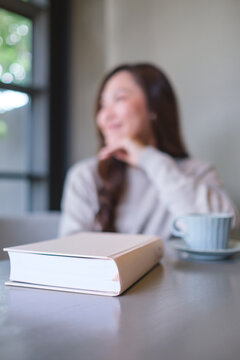Blurred image of a woman with a book and coffee cup on the table