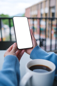 Vertical mockup image of a woman holding and using mobile phone with blank desktop screen in cafe