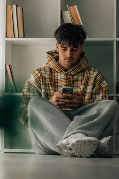 young man at home with mobile phone sitting on the floor