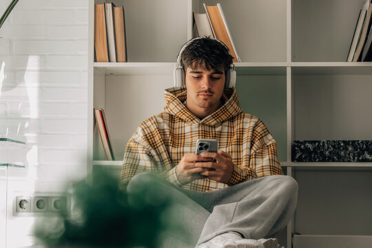 young man with headphones and mobile phone sitting on the floor indoors