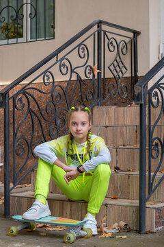 Skater girl sitting on stairs of urban building. Concept: Back to school youth street fashion and active autumn lifestyle. 