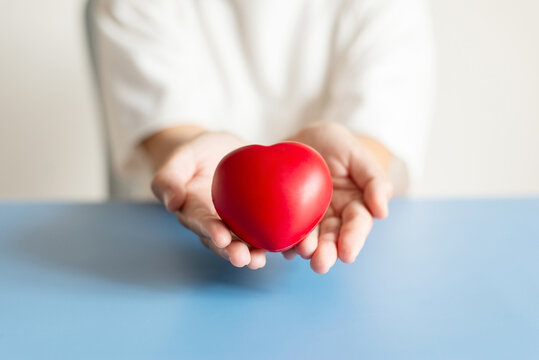 Close up of hands holding red heart on blue background for charity and healthcare concept