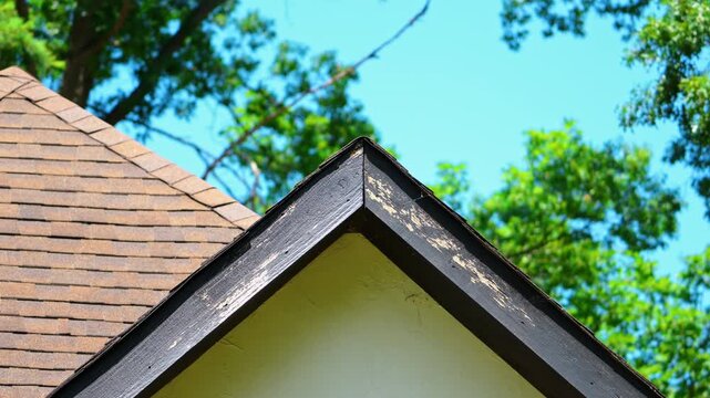 Residential roof gable with weathered wooden fascia and trim showing peeling paint and exterior wear.
