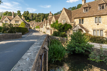 Fototapeta premium Scenic winding road through Castle Combe featuring iconic limestone houses and greenery, Cotswolds, England