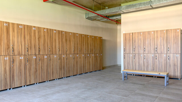 Spacious locker room featuring rows of contemporary wood finish lockers with numbered doors and handles. Complemented by a comfortable bench