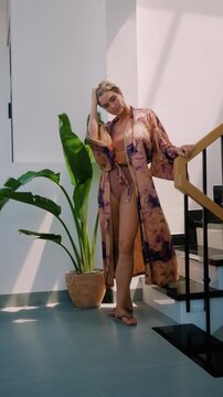 Elegant woman wearing luxury kimono robe over  swimsuit in modern tropical villa.