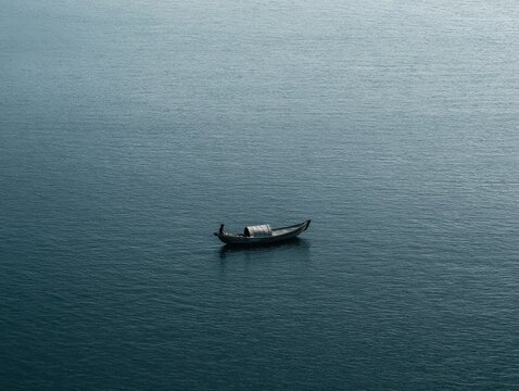 A lone fisherman rowing a small wooden boat across the calm, deep blue water of a vast river