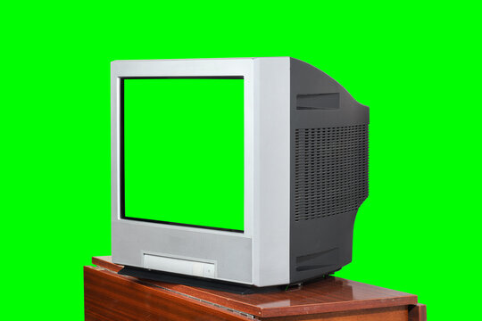 An old green screen television sits on a vintage 1990s, 1980s stand against a green background.