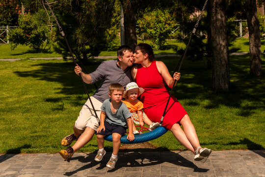 Parents Kissing While Children Sit on Playground Swing