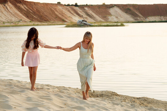 Smiling Mother Walking Barefoot With Young Daughter Beside Lake