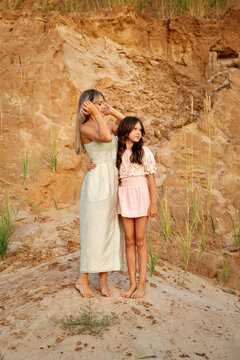 Mother Adjusting Hair While Daughter Stands Beside Sandy Cliff