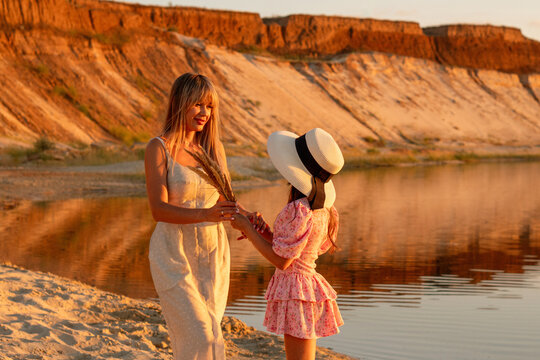 Mother And Daughter Holding Hands Beside Sunset Lake