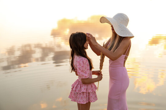 Mother Adjusting Daughter Hair Beside Sunset Lake