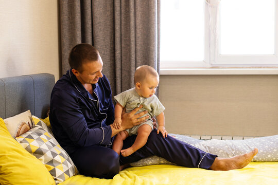 Father Supporting Baby Son Sitting On Bed At Home