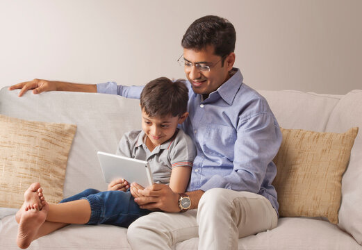 Father and son using digital tablet on sofa