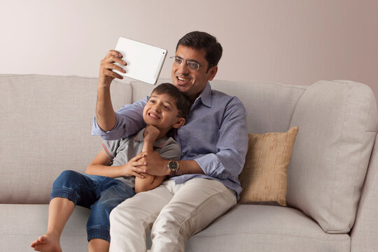 Happy father and son using digital tablet on sofa at home