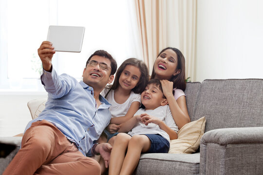 Happy young family taking selfie with digital tablet in living room sofa