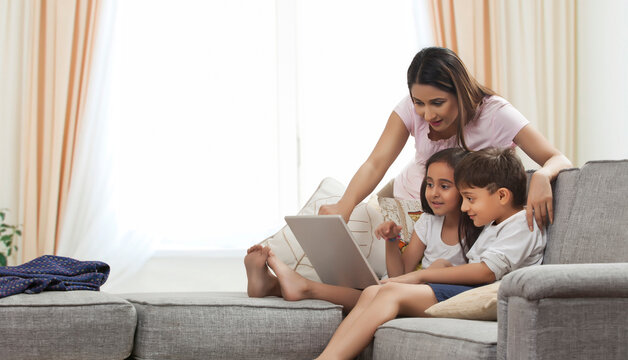 Mother watching children using laptop in living room