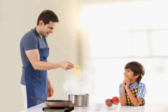 Father and son preparing noodles in kitchen