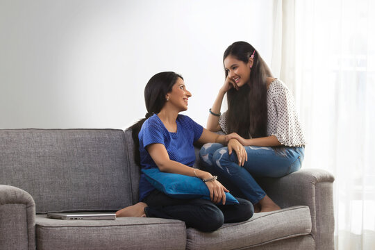Mother talking to her daughter sitting on sofa in living room
