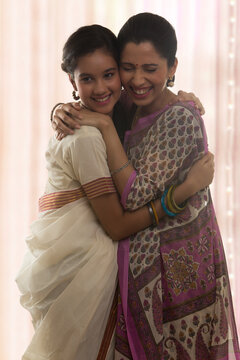 Smiling teenage daughter in sari and mother hugging 
