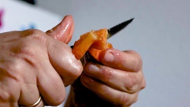 Woman slicing very ripe juicy peach with a small knife over a metal mixing bowl. Home cooking with copy space.