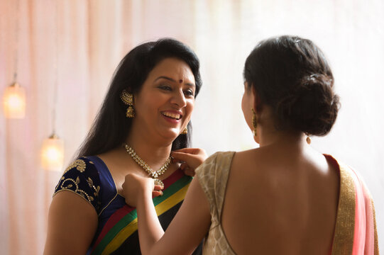 Daughter helping her mother in wearing necklace