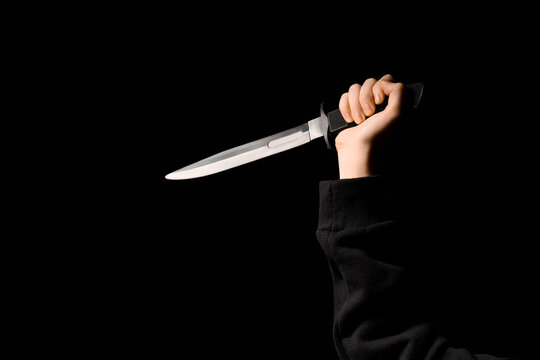 Hand holding a sharp hunting knife with a black handle, crime and violence concept, isolated on a dark background