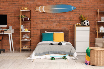 Teenage boys bedroom with brick wall surfboard decor gaming accessories and modern furniture for a youthful interior design © Pixel-Shot