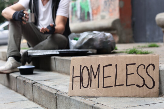 Homeless person sitting on city steps with a cardboard sign asking for help, poverty and social issues