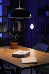 Stack of white paper tied with twine and a closed laptop on a wooden table under a pendant light in a dark room, a black pendant light illuminates the workspace, casting a warm glow on the items below © Pixel-Shot